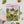 A flat-lay of a 'Walking Logbook' featuring a whimsical landscape illustration with daisies, a cliff edge with a lighthouse, and a purple sky. The book is styled on a light gray surface with a pencil, wooden pencil sharpener, a pink card, and other small decorative items.