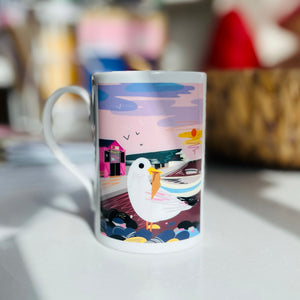 Mug with a colourful design of a seagull on Seaford Beach eating an ice cream with Seaford head cliffs in the distance.
