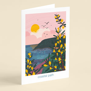 Greeting card with a coastal path illustration with gorse flowering, the sea and a pink sky and cliffs in the background