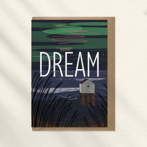 A beach hut on stilts on a night time beach with the northern lights and DREAM in large letters illustration by onneke