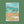 A greeting card set titled 'the Christmas swim' by Onneke, featuring a winter illustration of swimmers in the ocean with a beige band across the middle and a sandy beach scene at the bottom, displayed on a textured green background.