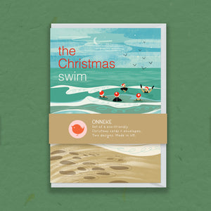A greeting card set titled 'the Christmas swim' by Onneke, featuring a winter illustration of swimmers in the ocean with a beige band across the middle and a sandy beach scene at the bottom, displayed on a textured green background.