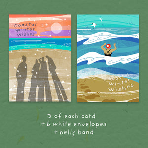Two illustrated winter beach cards on a green textured background, with text below reading '3 of each card +6 white envelopes + belly band'. The left card shows silhouetted figures on a beach under a sunset sky, and the right card shows a person jumping into waves above a beach scene.