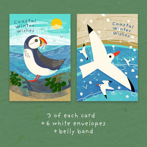 Two illustrated greeting cards with coastal winter artwork are shown side by side on a green textured background. The left card features a puffin with the text 'Coastal Winter Wishes'; the right card shows a white bird flying over blue water with smaller birds and the same text.