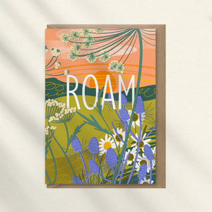 Greeting card with floral design and 'ROAM' text, a path in the background, the sun setting and wild flowers filling the card that was illustrated by onneke