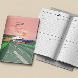 Running logbook with pink cover and open to lined pages on a beige background