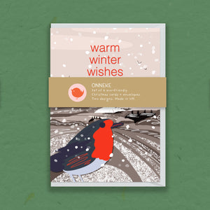 A greeting card package titled 'warm winter wishes' by ONNEKE, featuring a winter illustration with a robin on a snowy landscape, shown against a textured green background.