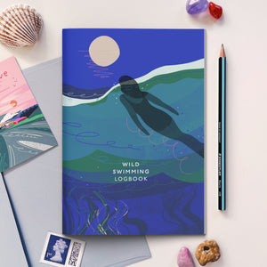 Wild Swimming logbook with the Full Moon Swim illustration on the cover and stationery and decorative items around it