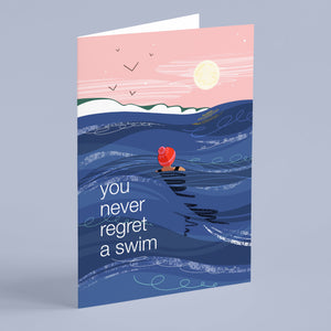 Greeting card with a swimmer in the ocean and a pink sky, featuring the text 'you never regret a swim'.
